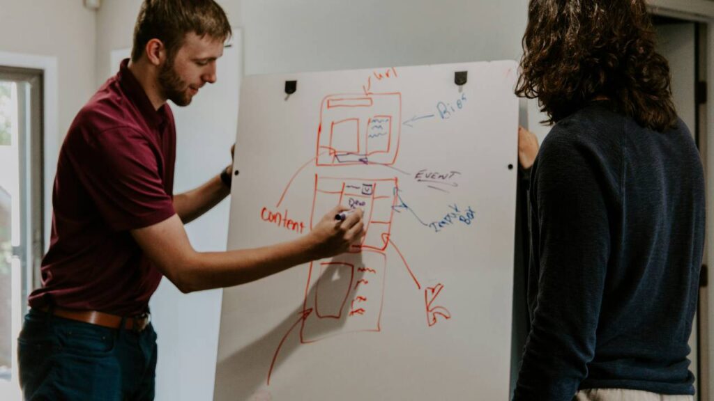 A woman and a man using a whiteboard to come up with a market research plan