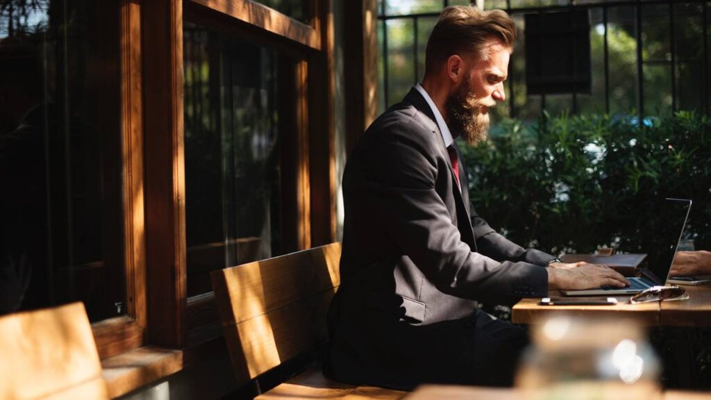 A man with a beard using a laptop in an outdoor setting