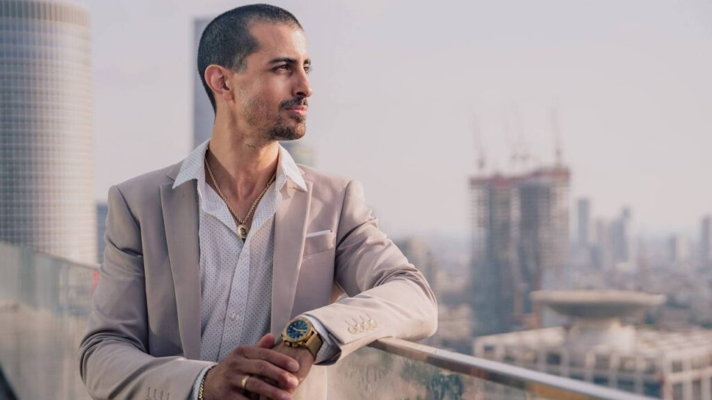 A businessman in a beige suit looking at the city from a balcony 