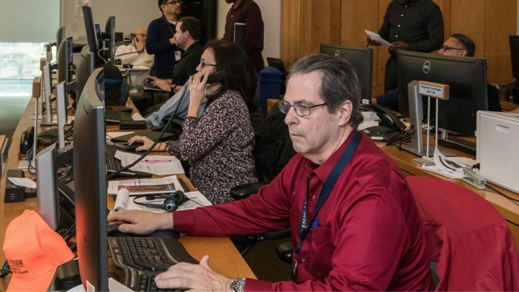 A middle-aged man in a red shirt working in an office setting 